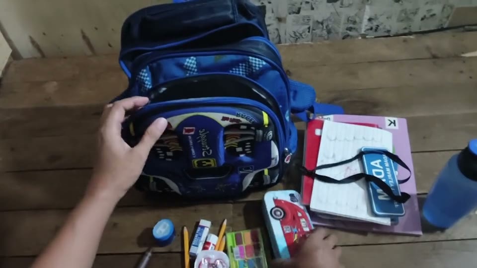 First-person view of two hands arranging school supplies inside a blue backpack.