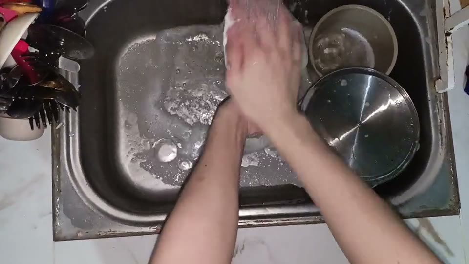 First-person view of two hands washing a plate in a kitchen sink.