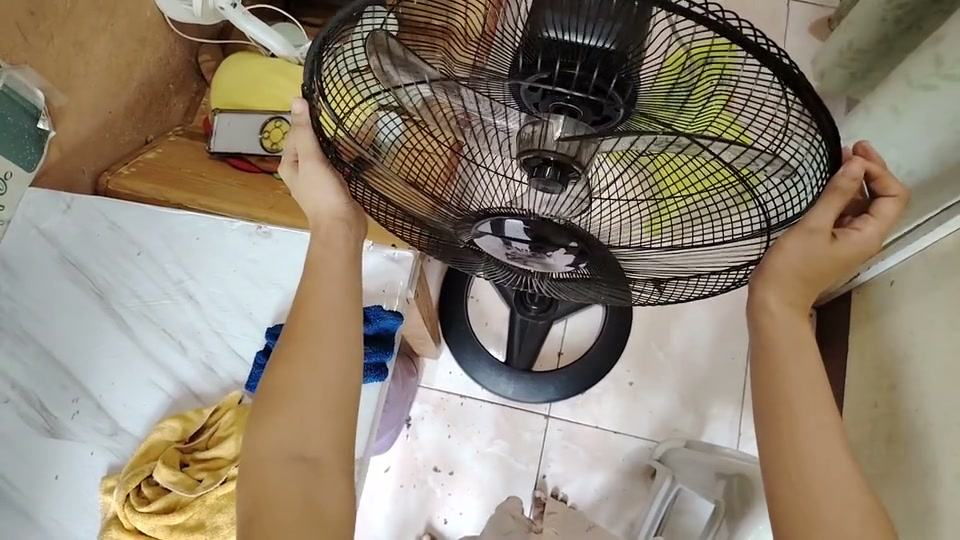 First-person view of two hands disassembling, cleaning, and reassembling an electric fan.