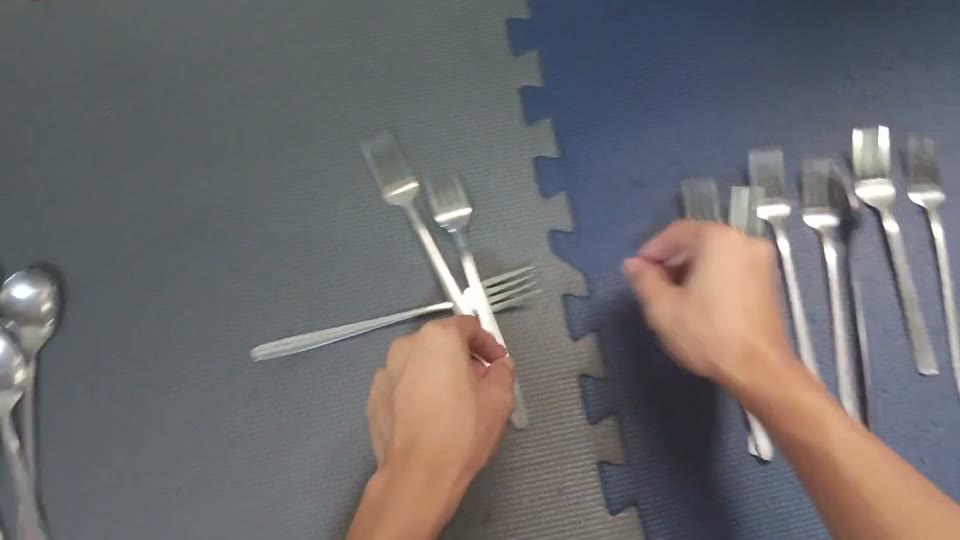 First-person view of two hands sorting metal forks and spoons on a dark mat.